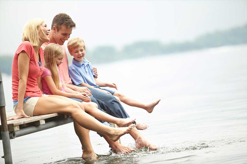 A family swinging their feet in a lake sitting on a dock in summer